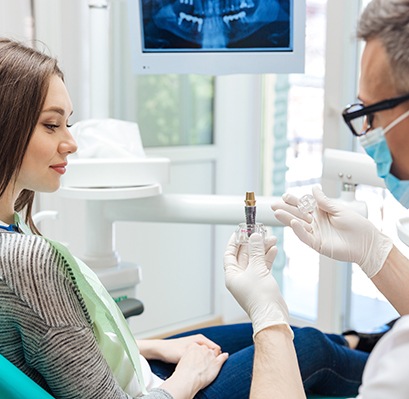 Dentist showing sample implant to woman in dental chair