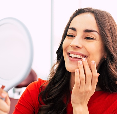 Woman in red-orange shirt admiring her smile in handheld mirror