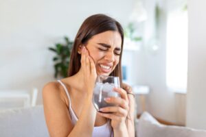 Woman drinking ice water and cringing because of sensitive teeth